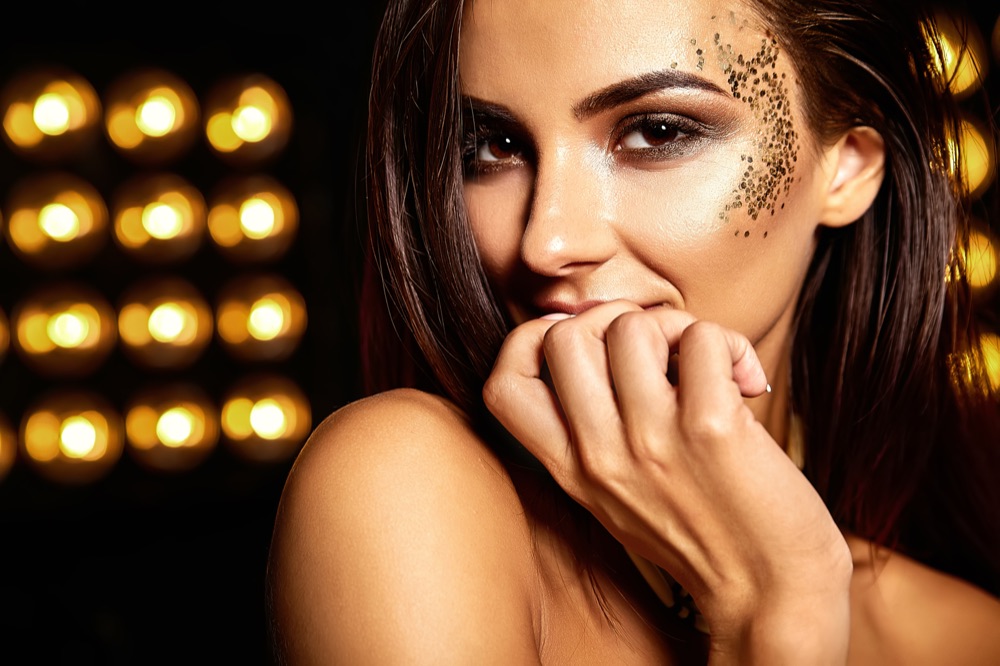 Beauty professional showcasing flawless makeup application with gold glitter accents